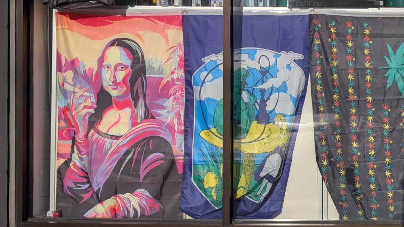 Flag of Mona Lisa smoking a joint next to a flag Alice and a hooka smoking catepillar as seen through the window of a smoke shop